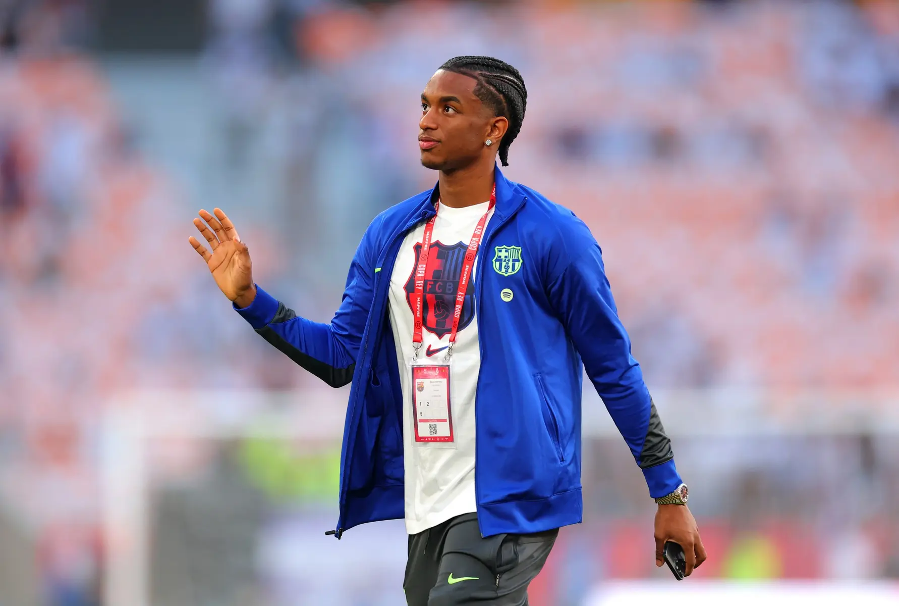 Alejandro Balde wearing a blue FC Barcelona jacket and white t-shirt on a soccer pitch