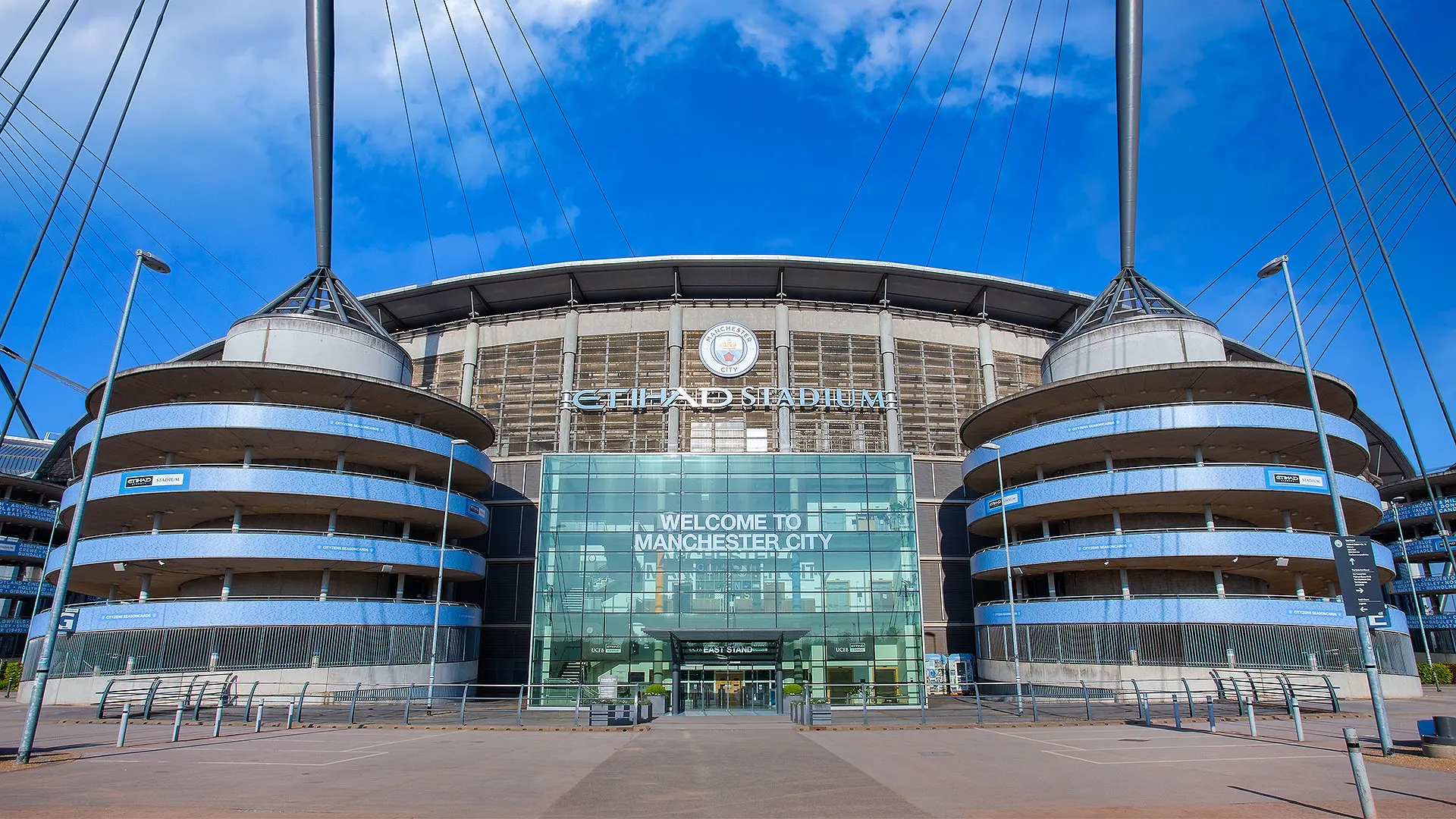 Wide shot of the Etihad Stadium exterior featuring the Manchester City crest and welcome signage