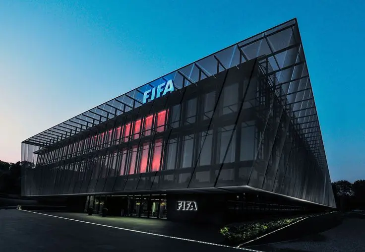 Modern glass exterior of the FIFA headquarters building at dusk with illuminated FIFA logos