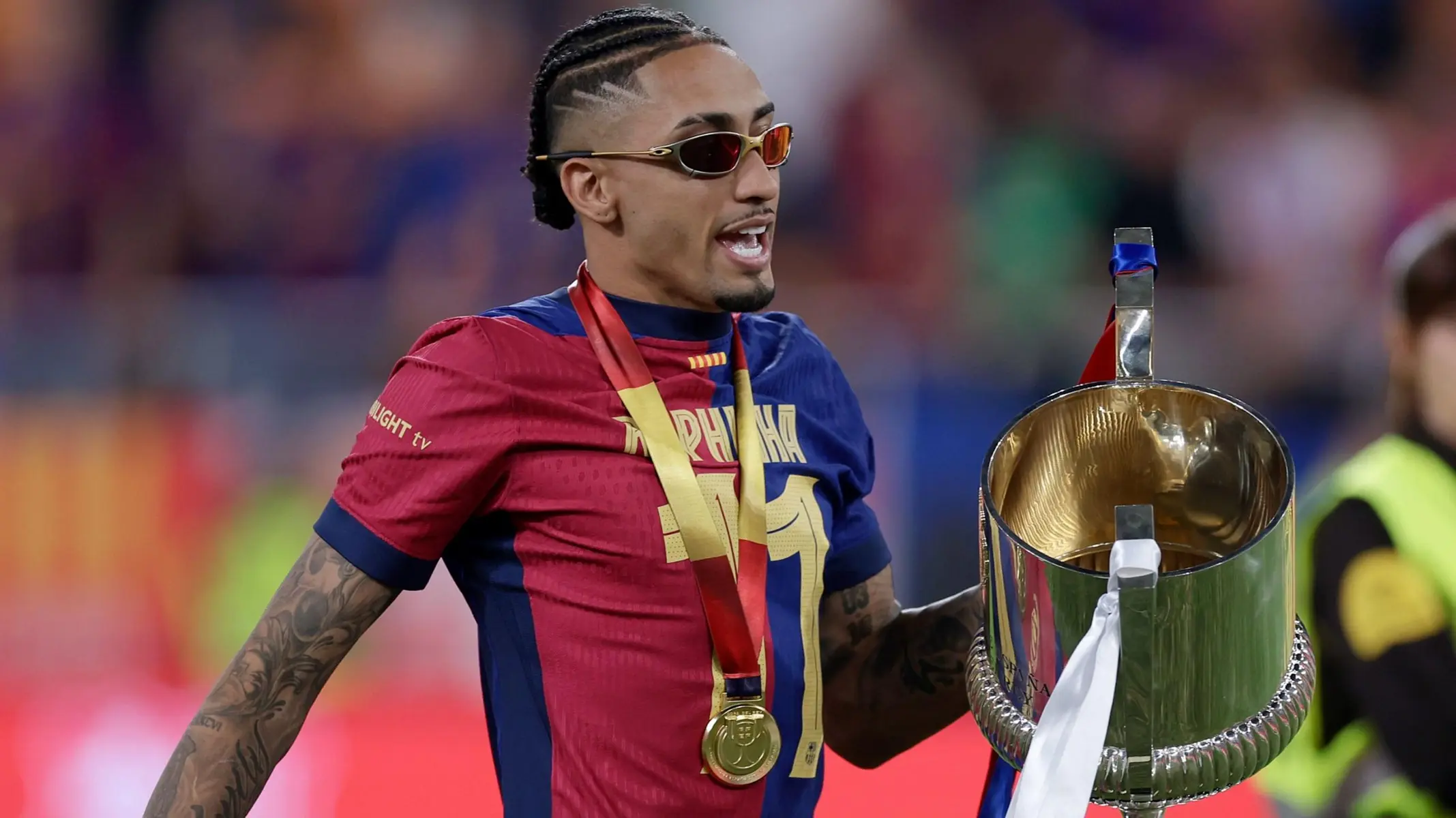 FC Barcelona winger Raphinha wearing sunglasses and a gold medal while holding a trophy