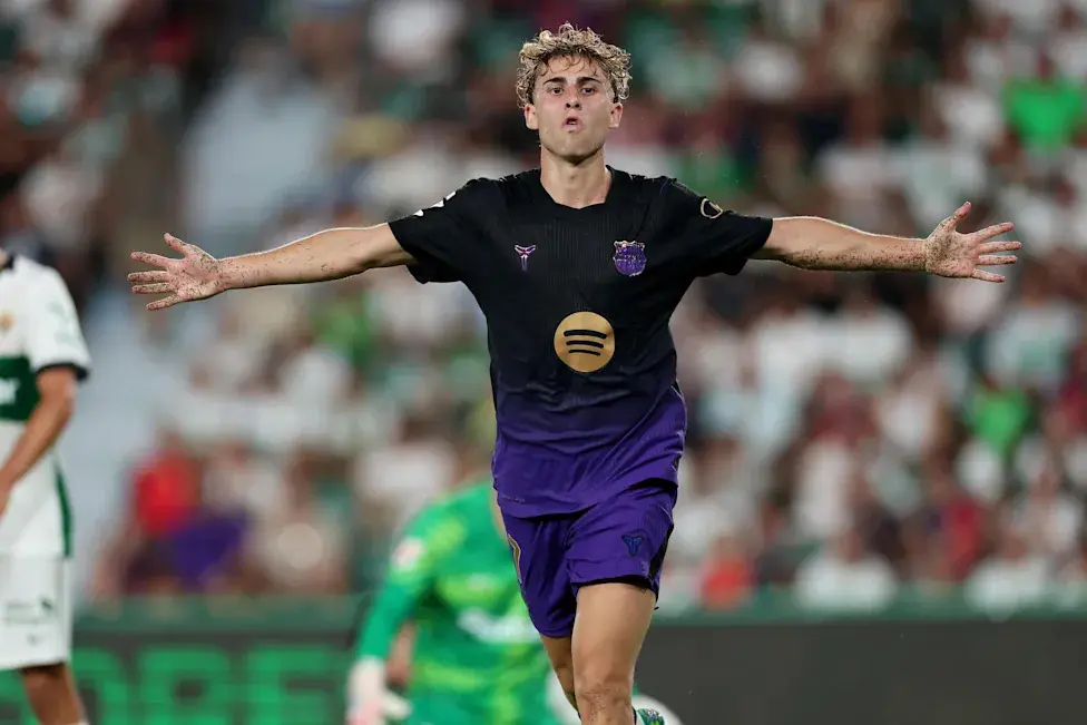 Fermin Lopez in a black and purple FC Barcelona kit celebrating with arms outstretched on the pitch