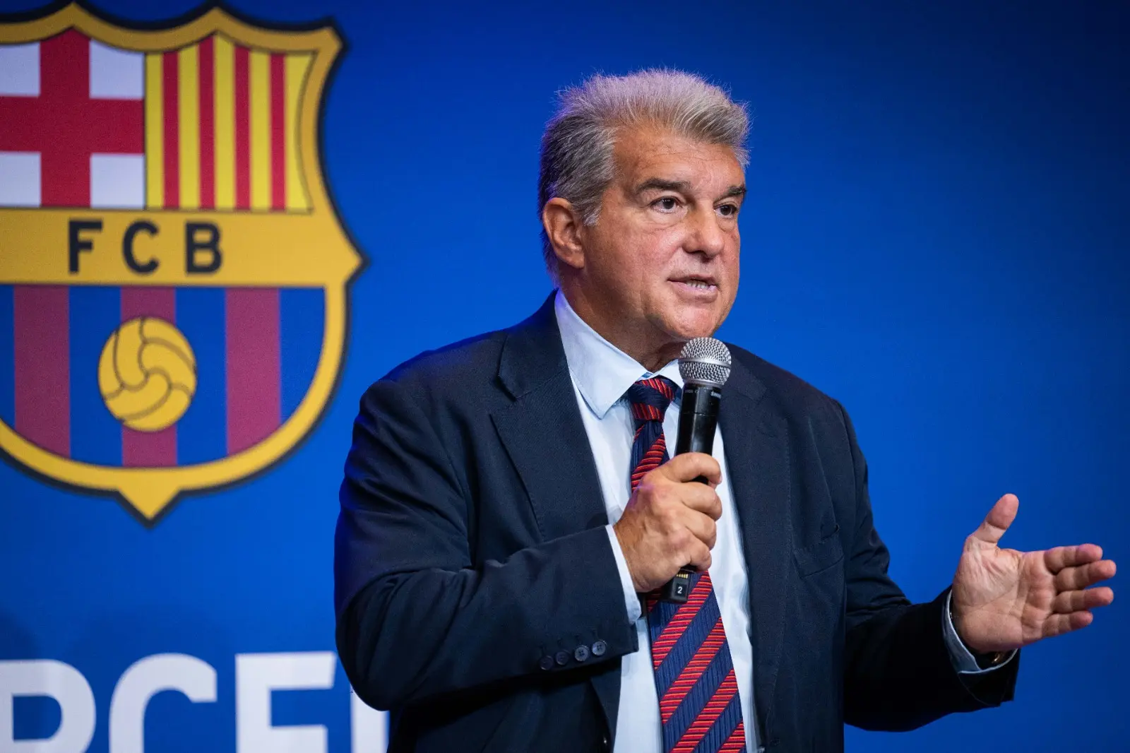 Joan Laporta speaking into a microphone in front of the FC Barcelona crest