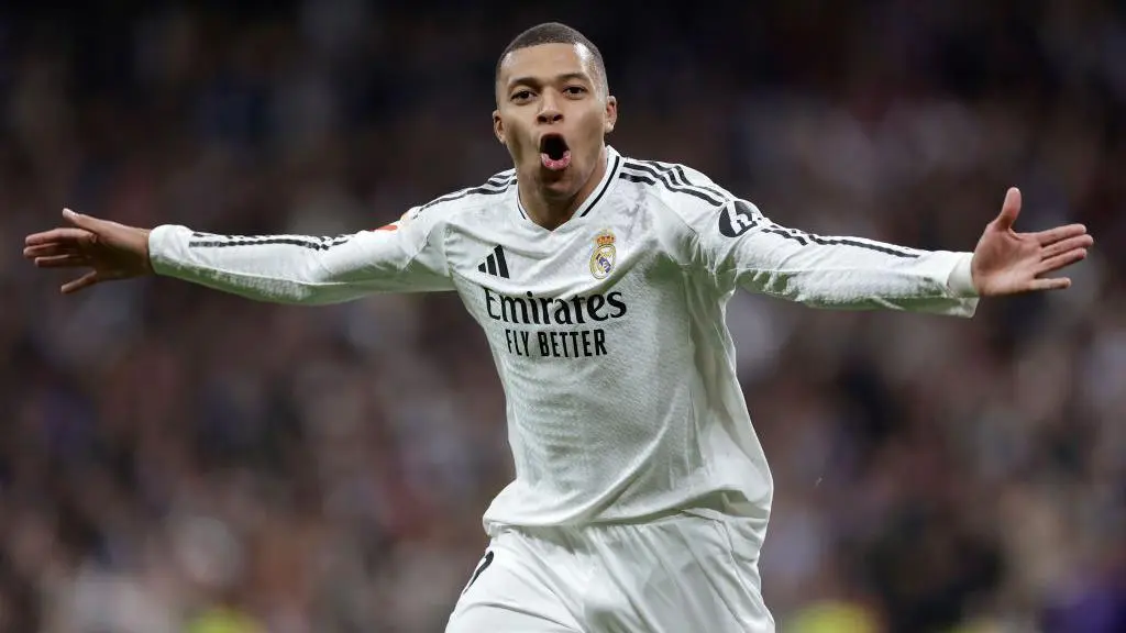 Kylian Mbappe in a Real Madrid home kit celebrating with arms outstretched and mouth open