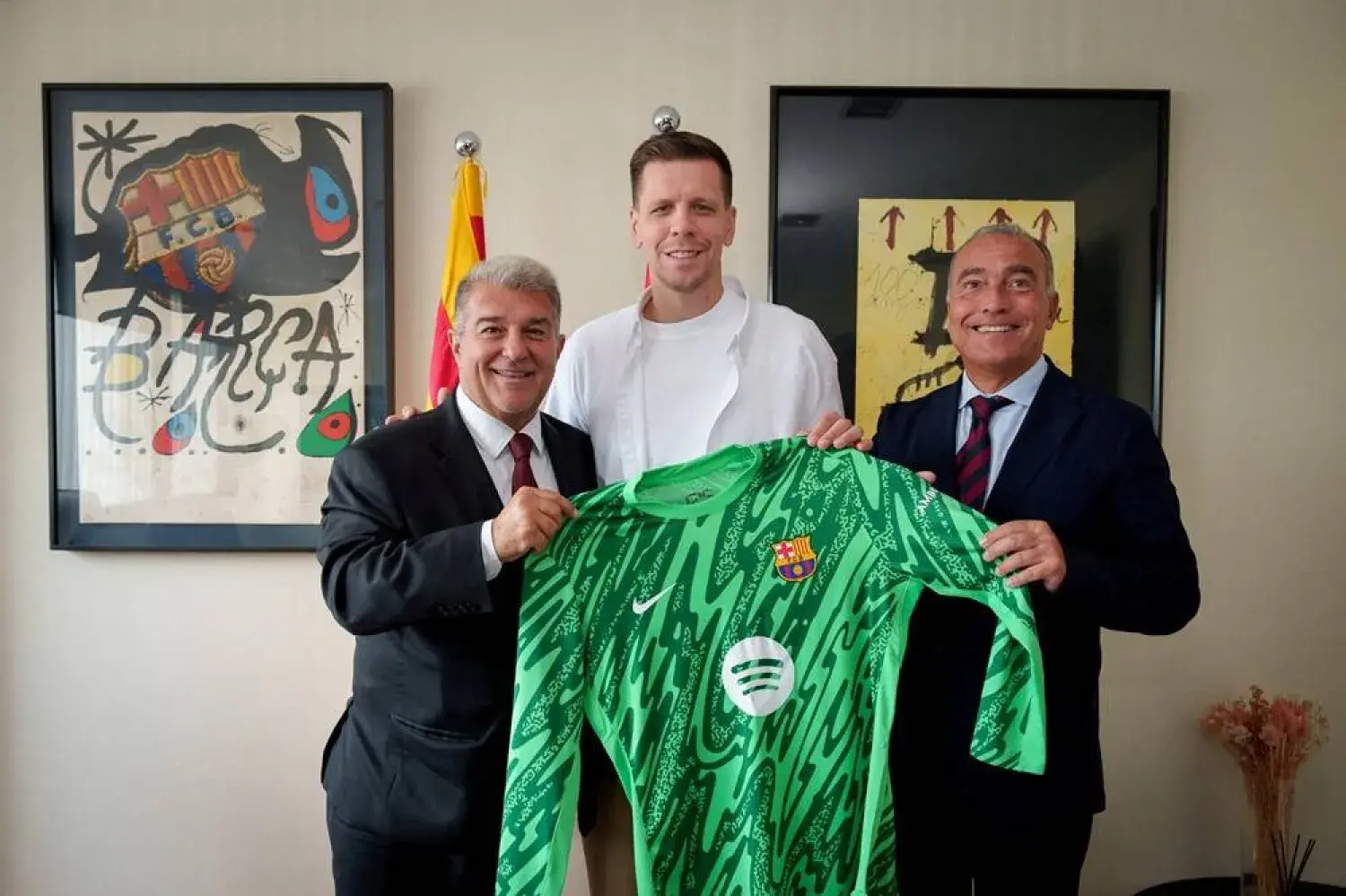 Wojciech Szczęsny standing with two executives holding a green FC Barcelona goalkeeper jersey