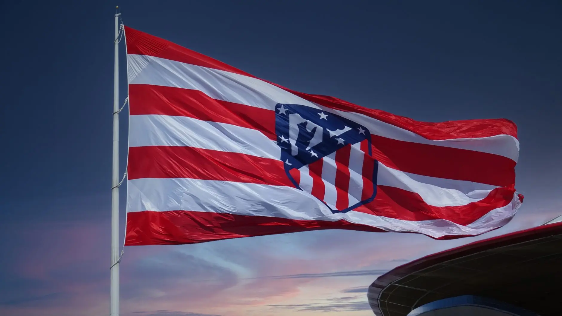 Atletico Madrid flag with red and white stripes and team crest waving against a twilight sky