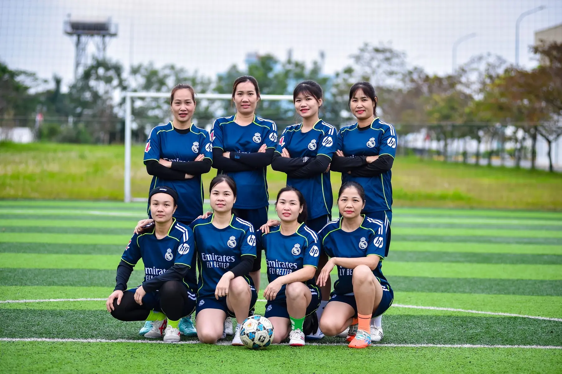 A group of eight female soccer players in dark blue Real Madrid kits posing on a green field.